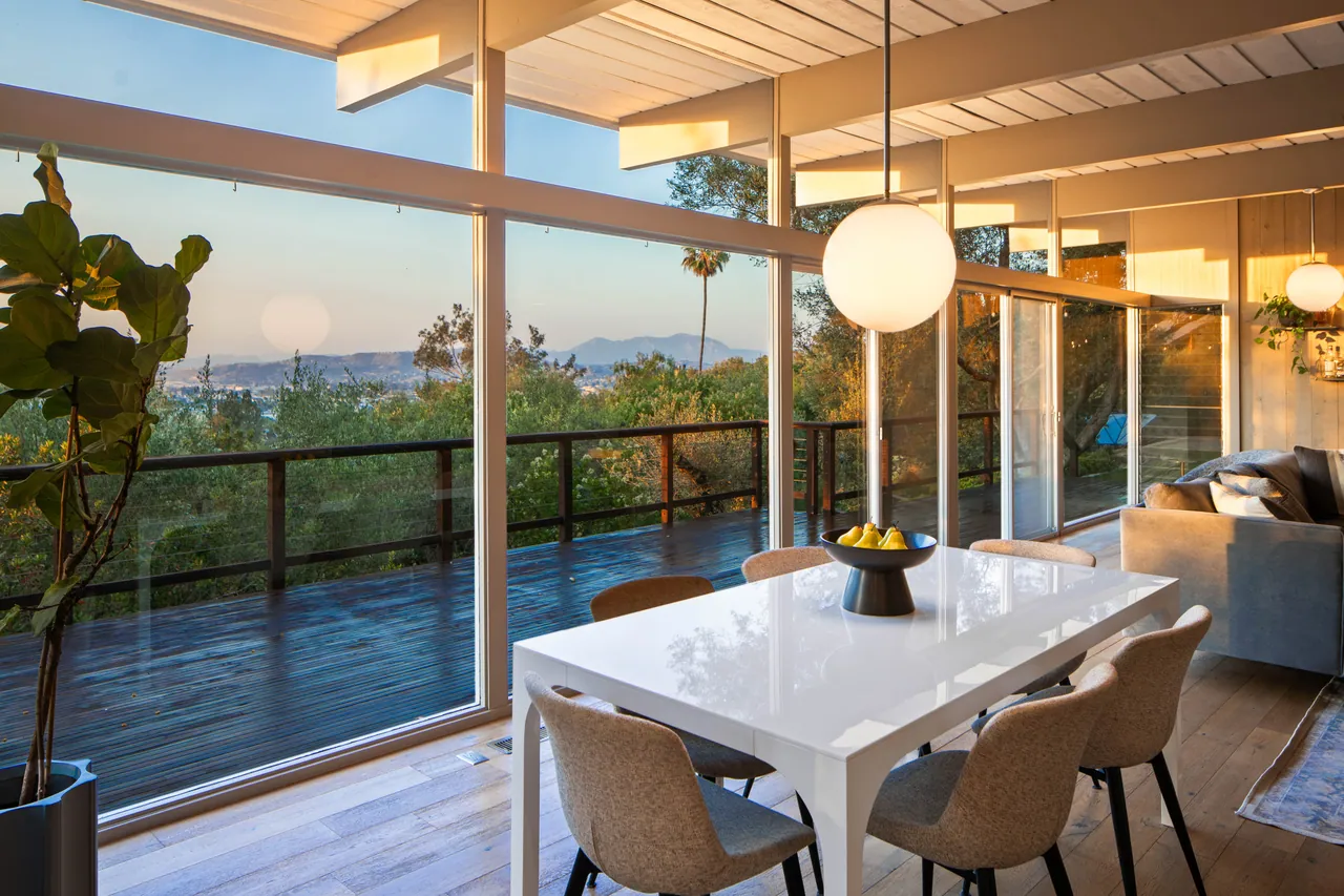 Dining table beside the wall of glass with the deck and valley beyond