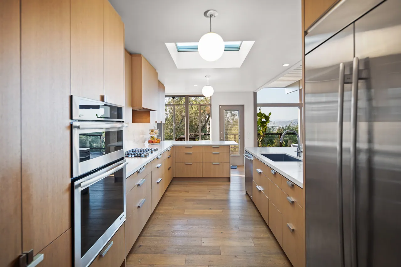 Galley view of the kitchen with wall ovens beneath a skylight