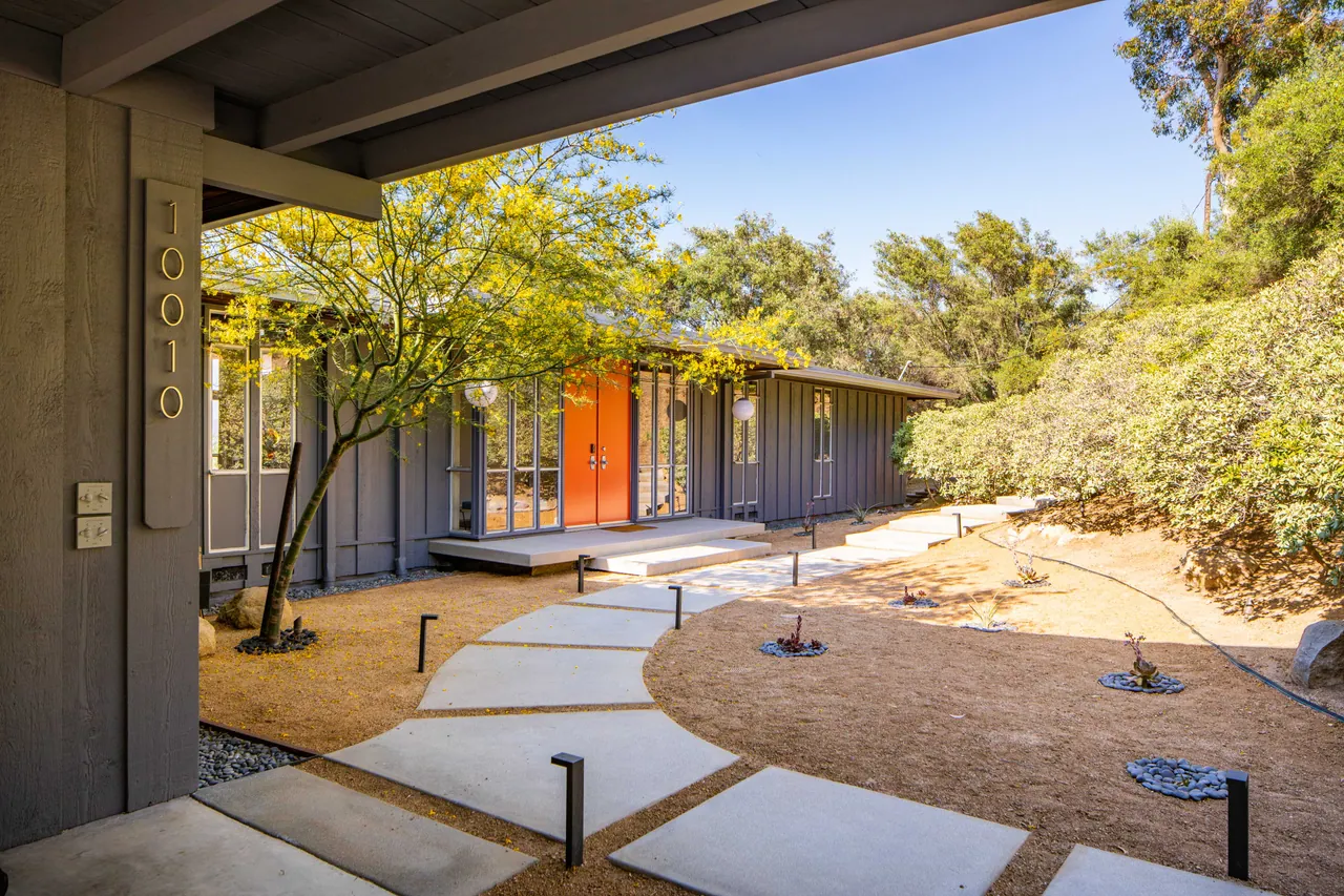 Concrete pavers cross the entry court toward the vermilion front doors