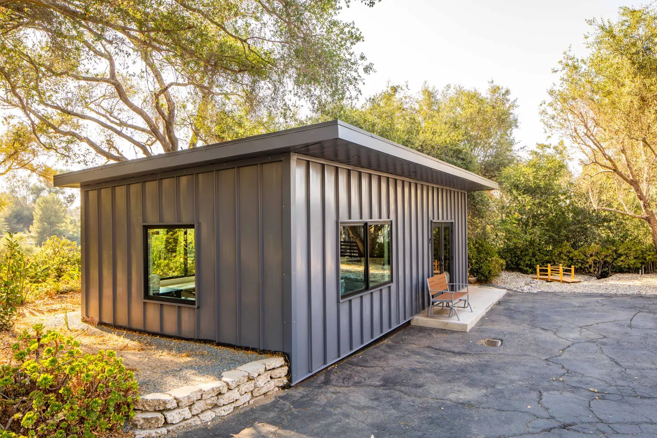 The office addition, clad in vertical metal siding among the oaks