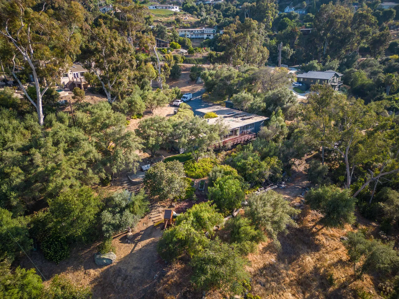 Aerial view from behind the house: the deck, the green and gardens in the foreground, the carport, office addition and driveway beyond